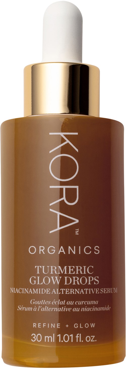 Bottle of KORA Organics turmeric glow drops serum with white dropper cap, gold collar, and brown bottle. Key product name visible.