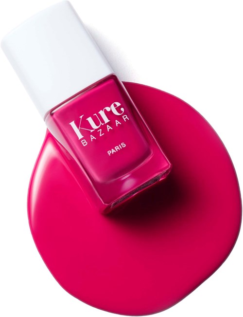 Een roze nagellakfles op een bijpassend roze oppervlak. Witte dop, merk 'Kure Bazaar' uit Parijs.