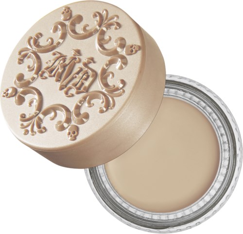En beige behållare med lock som har utsmyckade mönster och initialerna 'KH'. Den innehåller en krämig substans.