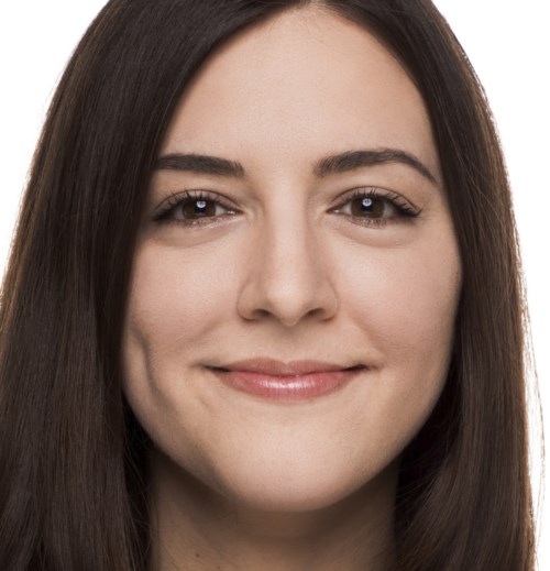 En kvinna med långt mörkt hår som ler lite, med klar hud och neutral bakgrund.