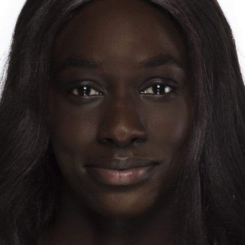En närbild av en kvinna med mörk hy och långt, svart hår, ler milt.