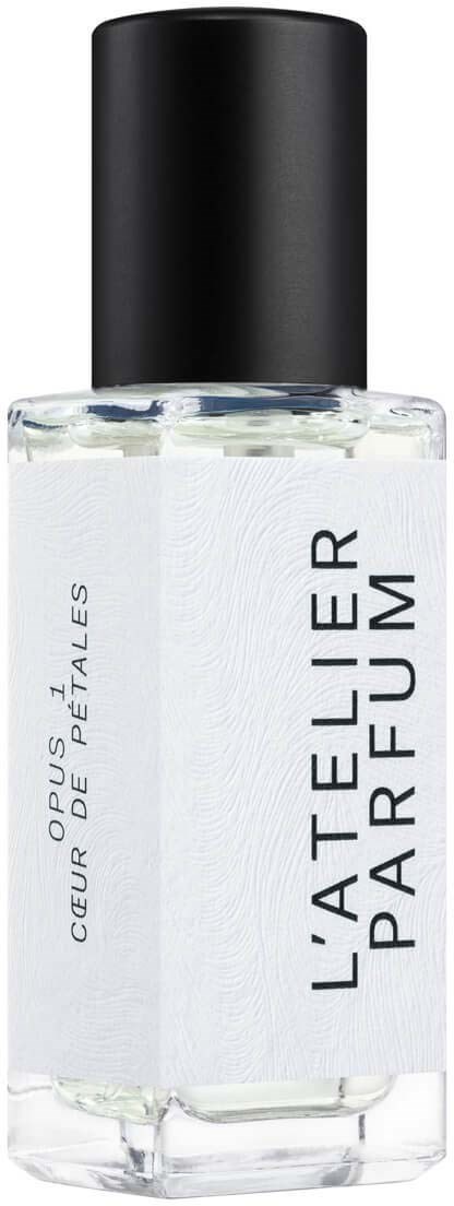 Przezroczysta butelka perfum z czarną nakrętką i białą etykietą, na której napisano "L'Atelier Parfum" i "Coeur de Pétales."