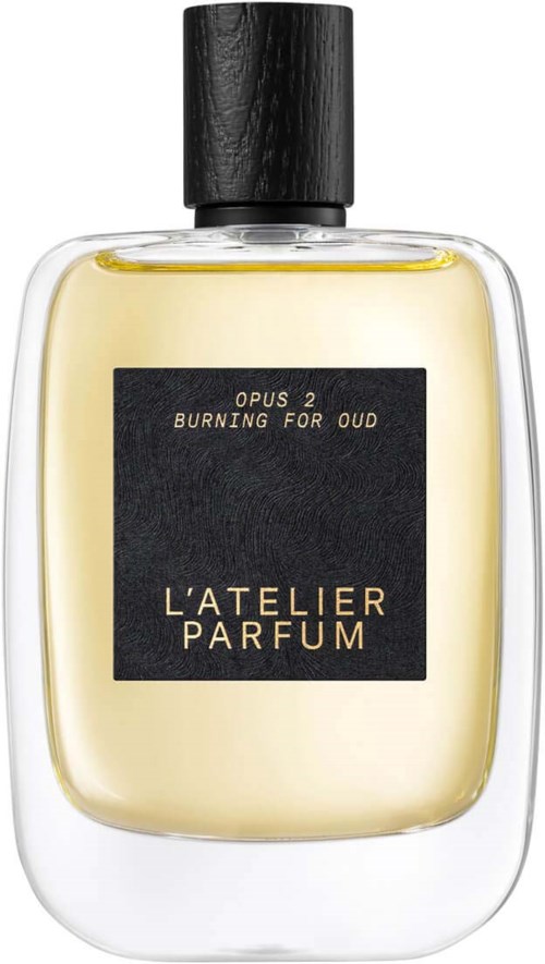 En parføneflaske med sort låg og mærke, der siger 'L'ATELIER PARFUM' og 'BURNING FOR OUD.'