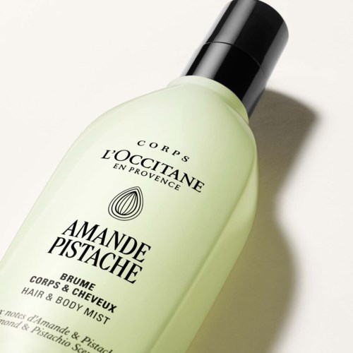 Ljusgrön flaska med svart lock, märkt L'Occitane Amande Pistache hår- och kroppsspray.