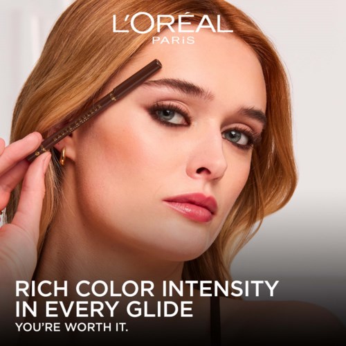 En kvinna med rött hår och makeup håller en ögonbrynspenna nära sitt öga, för att marknadsföra L'Oréal Paris sminkprodukter.