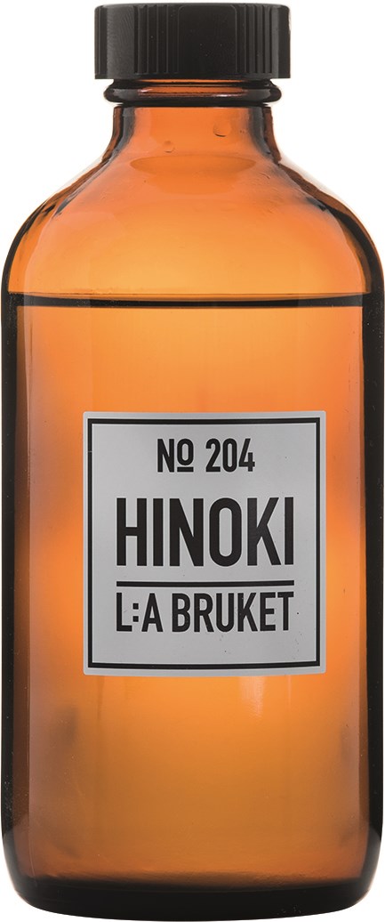 En brun glasflaske med sort låg, mærket 'No 204 Hinoki L:A Bruket'.