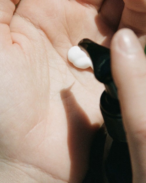 A hand holding a black bottle with white cream being dispensed onto the palm.