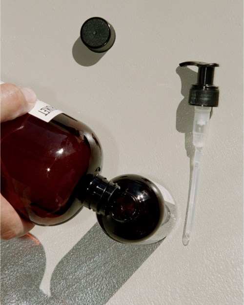 A person is pouring a dark liquid from a bottle into a socket with a dropper nearby on a white surface.