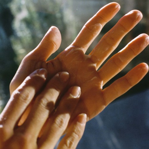 Two hands gently touch fingers, with a soft natural background, creating a warm and peaceful scene.