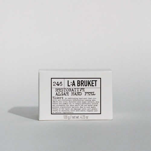 A small white box labeled 'L:A BRUKET,' containing 120g of hand peel with restorative ingredients and elderflower.