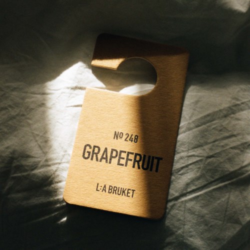 A wooden door hanger with the words "Grapefruit" and "L:A Bruket," illuminated by sunlight.