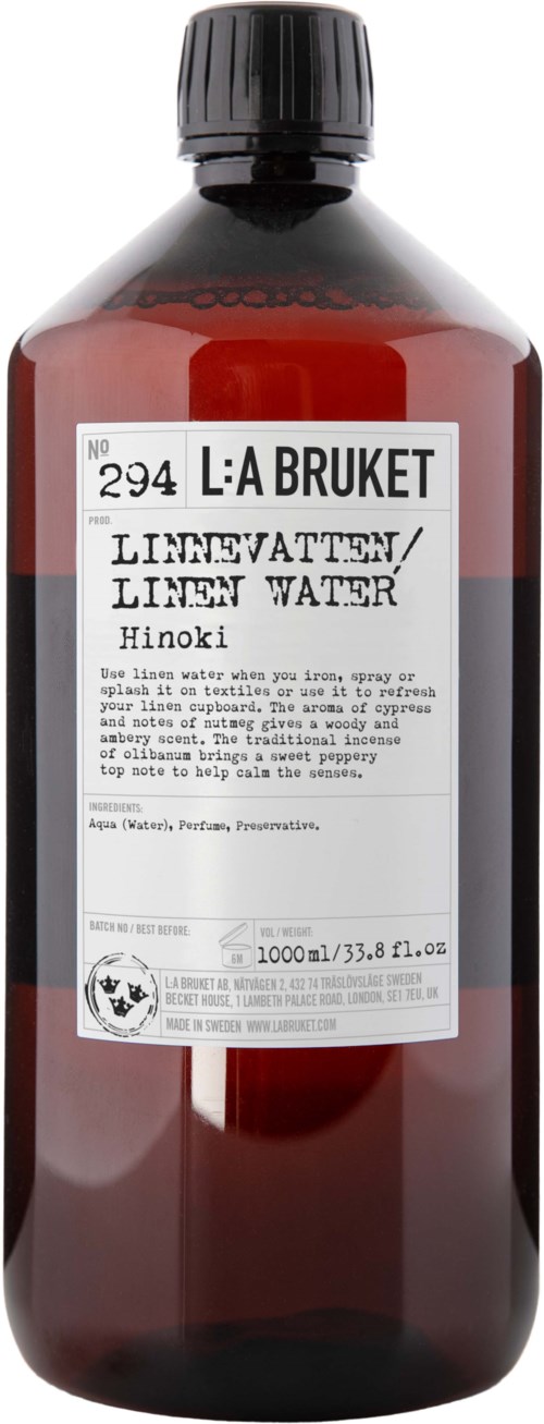 A brown bottle with a black cap, has a white label with text, including 'L: A BRUKET' and 'LINEN WATER Hinoki'.