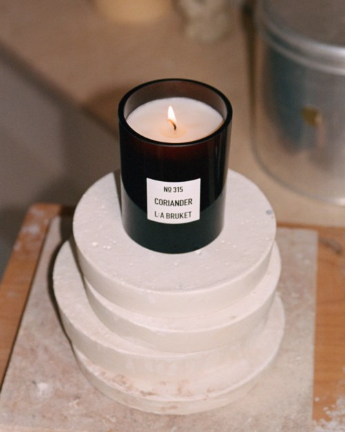 A white three-tier cake with a black candle labeled Coriander on top, placed on a wooden tray.