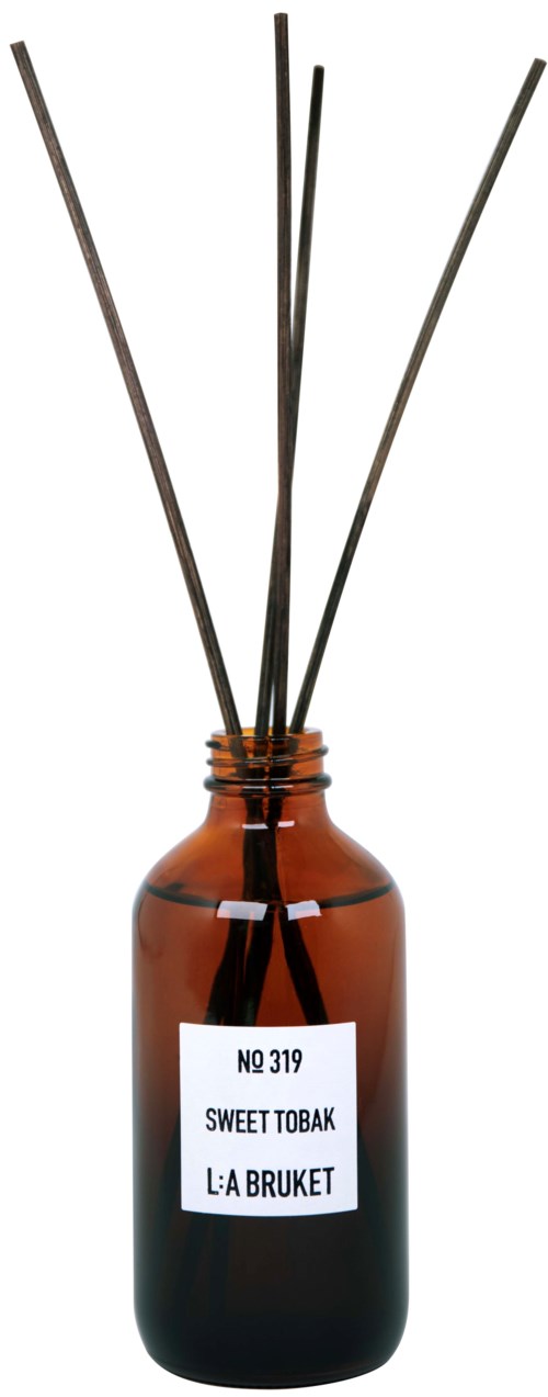 A brown bottle with a white label and black reed sticks inside, used as a reed diffuser.