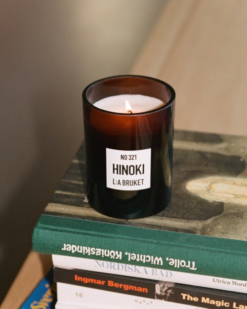Een brandende kaars in een donker glas op een stapel boeken op een houten oppervlak.