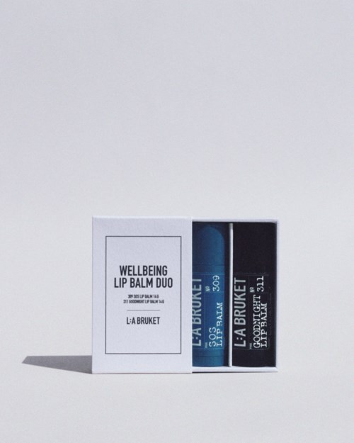 A white box contains two lip balm sticks, one blue and one black, labeled 'Wellbeing Lip Balm Duo' and 'La Bruket.'