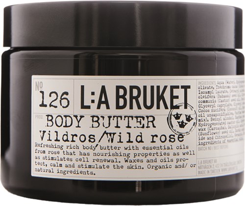 En svart burk med vit etikett visar kroppssmörj med vildros, närande oljor och organiska ingredienser.