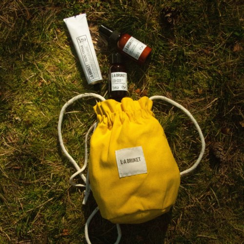 A yellow drawstring bag with skin care bottles and a tube placed on grass.