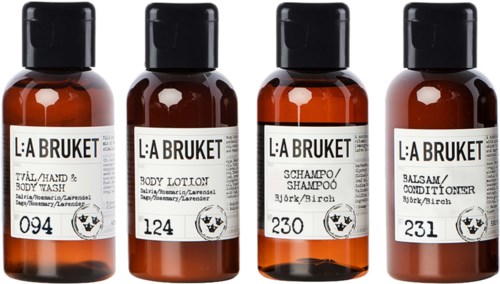 Fyra små bruna flaskor märkta med bad- och kroppsvårdsprodukter. De innehåller schampo, kroppslotion och balsam.