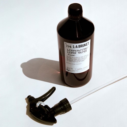 A dark bottle labeled 'L:A BRUKET Limevatten' with a spray nozzle, lying on a white surface.