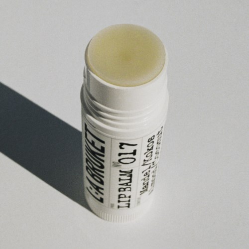 Lip balm tube with a yellowish balm on top, casting a shadow on a plain background.