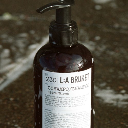 A dark brown shampoo bottle with a pump sits on a muddy ground.