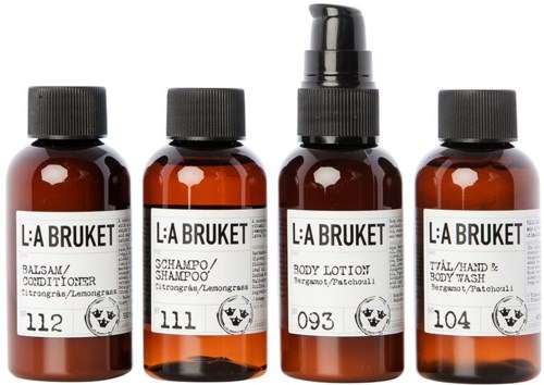 Fem små bruna flaskor med svarta lock, märkta för hår- och kroppsvårdsprodukter, inklusive balsam, schampo, lotion och tvätt.