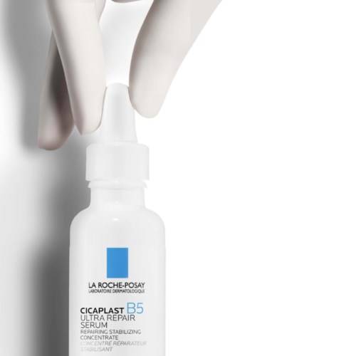 A small white bottle labeled La Roche-Posay with blue logo, held by a hand wearing gloves.