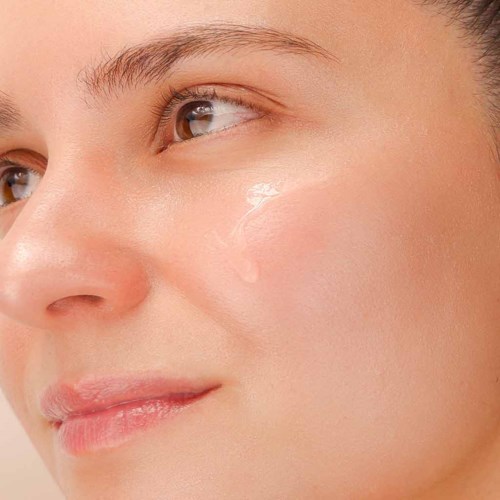 Nahaufnahme eines Frauengesichts mit klarer Haut, braunen Augen und sanftem Lächeln.