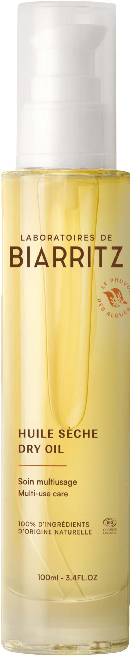 Eine klare Flasche mit weißen Pumpen, gelbe Flüssigkeit innen, Text über Trockenöl von Biarritz.