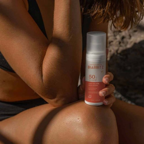 Eine Person hält eine Flasche Biarritz SPF 50 Sonnencreme im Sonnenlicht im Freien.