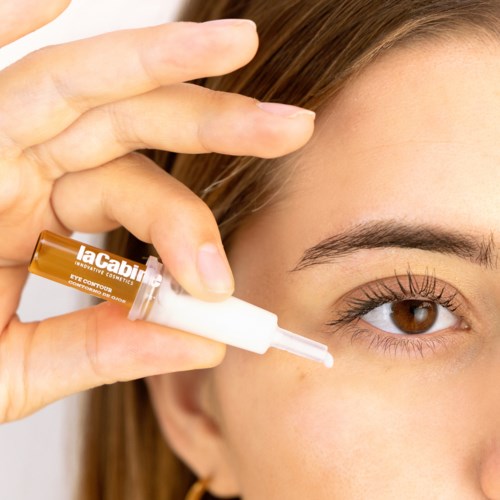 A person applies eye serum with a dropper to their under-eye area, focusing on skincare. The product is labeled LaCabina.