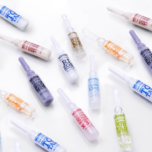 Olika små flaskor med tatueringfärg eller pigment i olika färger utspridda på en vit yta.