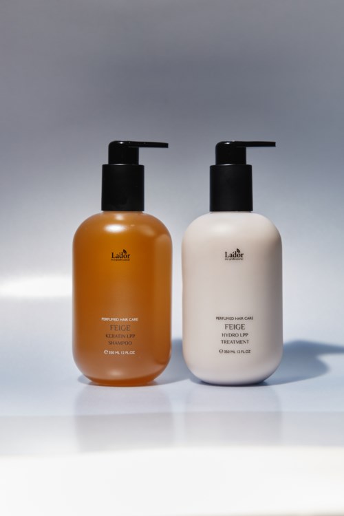 Two bottles, one orange and one white, with pump tops stand side by side on a light background.