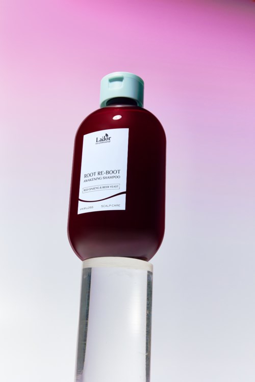 En flaska hårschampo med titeln 'ROOT RE-BOOT' på en vit stång med en rosa och lila bakgrund.