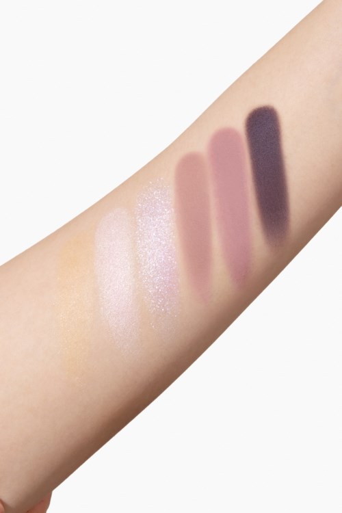 Swatches av forskjellige øyenskyggefarger på en persons arm, inkludert lyse, rosa og mørke nyanser.