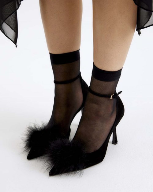 Black high heel shoes with furry tips worn with sheer black socks. The shoes are stylish and elegant.