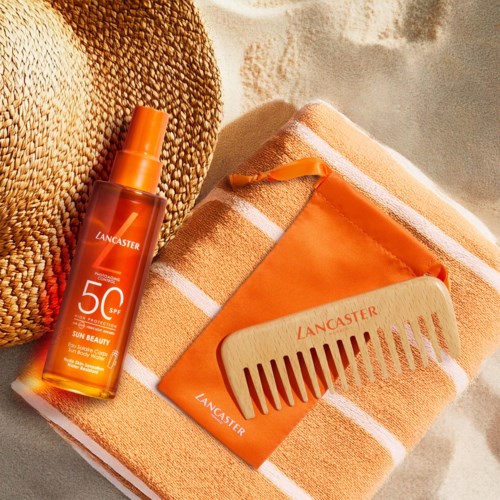 Ein Sonnenschutzspray, orange Geldbörse, Kamm und ein beiges Handtuch liegen am Strand.