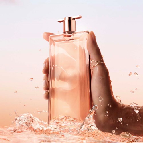 Eine Hand hält eine rosa Parfümflasche mit Wasserspritz, vor einem sanften Pastellhintergrund.