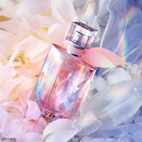 Ein rosa Parfühflasche mit rosa Schleife umgeben von weißen und pinken Blumen.