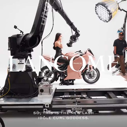 Een vrouw in een jurk op een roze motorfiets terwijl een robotarm haar filmt, met lichten en crew in de buurt.