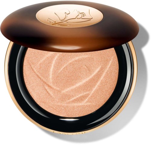 En kompaktpuder i en glänsande, rund svart och guld behållare. Locket har ett gyllene emblem. Inuti syns beige pressad puder.