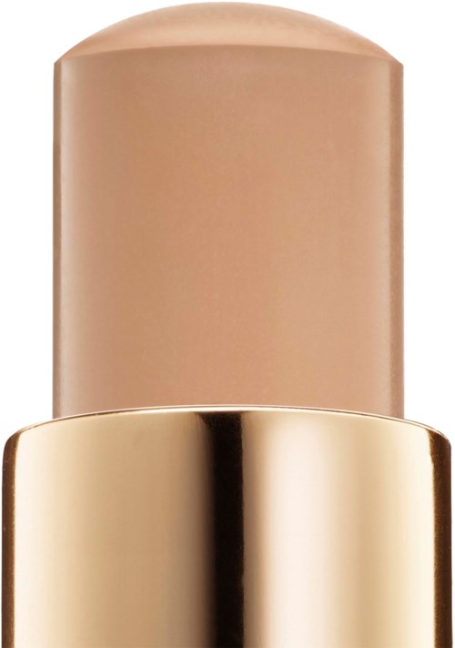 En beige pind med guldhætte, sandsynligvis et kosmetik- eller hudplejeprodukt.