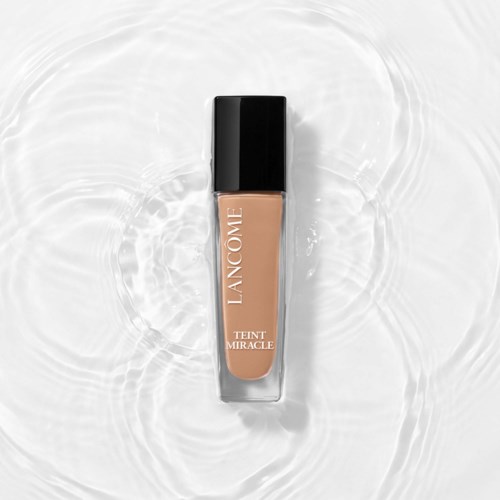 En beige flytende foundation i en klar flaske med svart lokk, merket "Lanc 4me Teint Miracle."