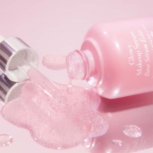 A pink bottle of makeup serum with spilled product and drops on a pink background.