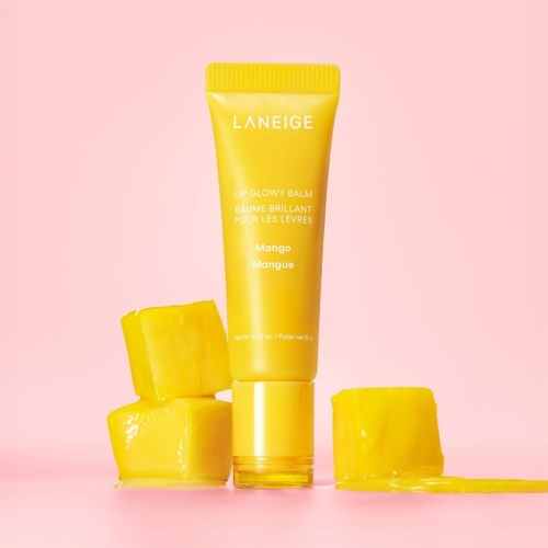 Gele tube van Laneige Mango Lip Glow Balm omringd door mango blokjes op een roze achtergrond.