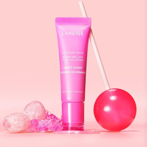 Eine pinke Tube mit Laneige Lip Glowy Balm, Süßigkeiten und ein pinker Lutscher daneben.