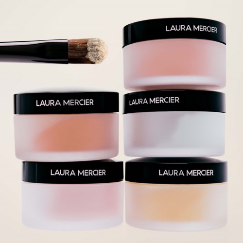 Sechs Laura Mercier Gesichtspuder in verschiedenen Tönen, angeordnet in einer Pyramide mit einem Pinsel in der Nähe.