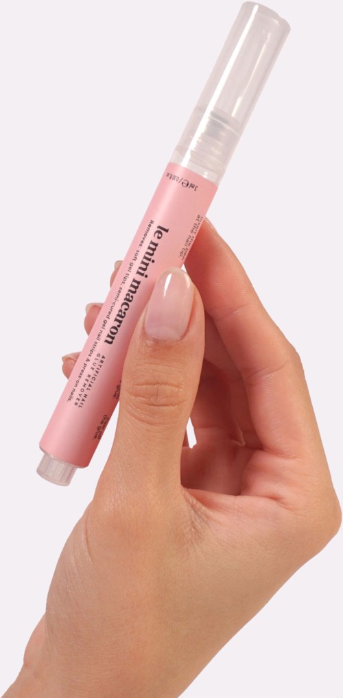 A hand holds a pink marker with a clear cap, label partially visible, against a plain light background.