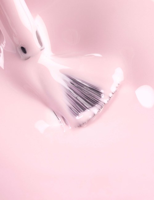 A paintbrush is being dipped in pink paint. The background is also pink with some light spots.
